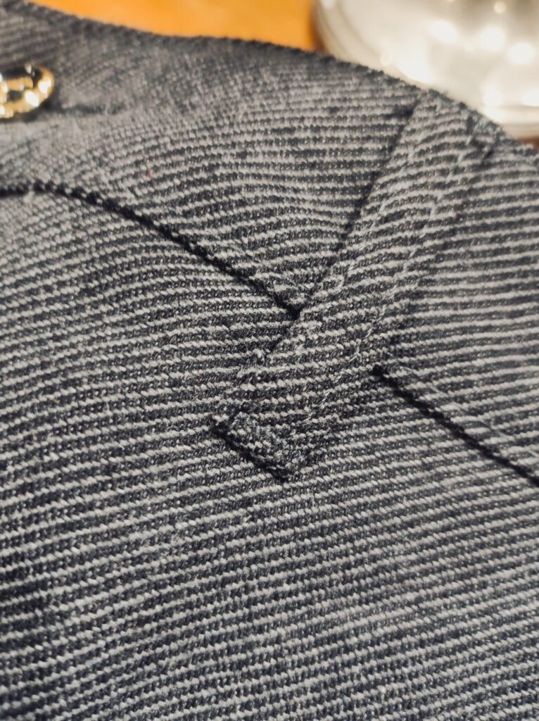 Nahaufnahme einer dunkelgrauen Hose mit feiner Struktur; Fokus auf Knopf, Gürtelriemendetail und dem hochwertigen, leicht elastischen Stoff.