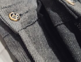 Nahaufnahme einer dunkelgrauen Hose mit feiner Struktur; Fokus auf Knopf, Gürtelriemendetail und dem hochwertigen, leicht elastischen Stoff.