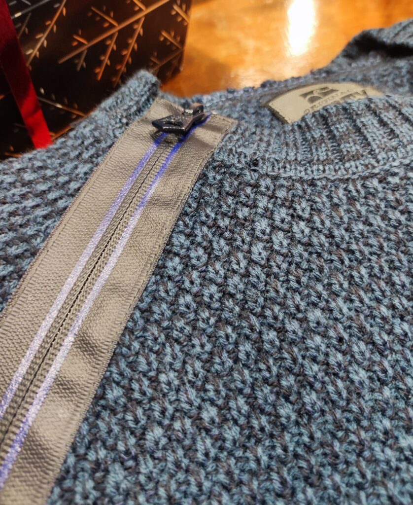 „Dunkelblauer Rusty Neal Herrenpullover aus hochwertigem Baumwoll-Mix, mit strukturiertem Strickmuster und dekorativem Reißverschluss-Detail an der Schulter, präsentiert auf einem Tisch bzw. einer Schaufensterpuppe.“