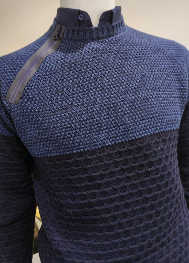 „Dunkelblauer Rusty Neal Herrenpullover aus hochwertigem Baumwoll-Mix, mit strukturiertem Strickmuster und dekorativem Reißverschluss-Detail an der Schulter, präsentiert auf einem Tisch bzw. einer Schaufensterpuppe.“