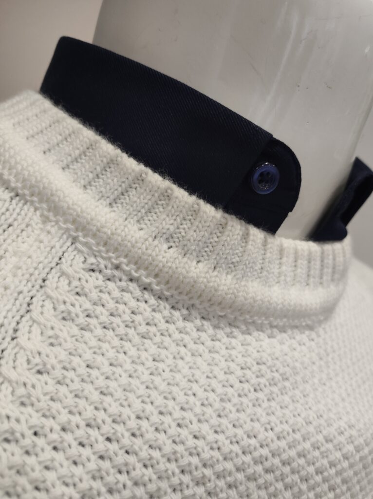 „Weißer Strickpullover auf einer Schaufensterpuppe, mit feiner Struktur und rundem Kragen, kombiniert mit dunkelblauem Hemd.“